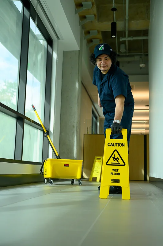 A male PCSI employee places a Wet Floor caution sign as he mops in a hallway.