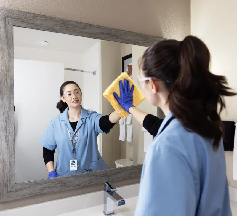 female housekeeper cleaning hotel bathroom mirror
