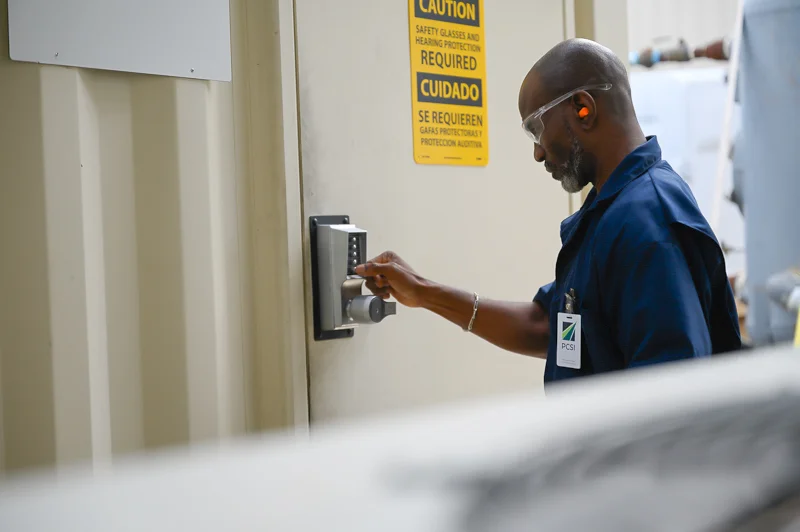 A male PCSI employee punches in the code to a secure facility. Caution signs are prominently displayed on the door.