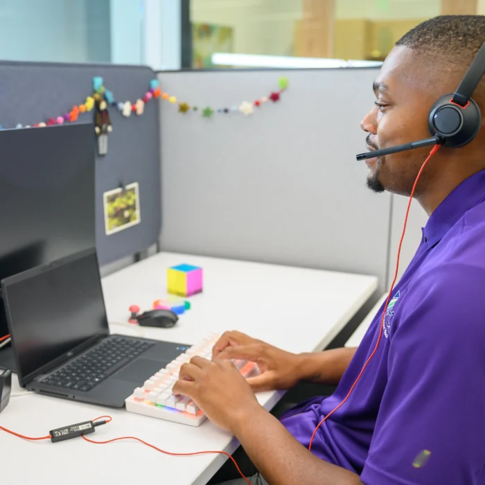 male employee is answering calls on a computer wearing an ear piece