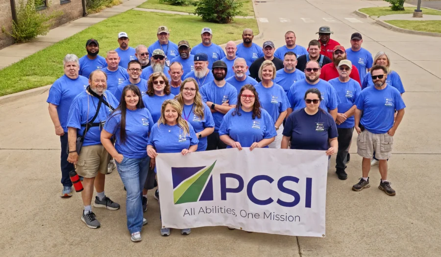 group of PCSI employees wearing blue shirts and showcasing a PCSI company banner