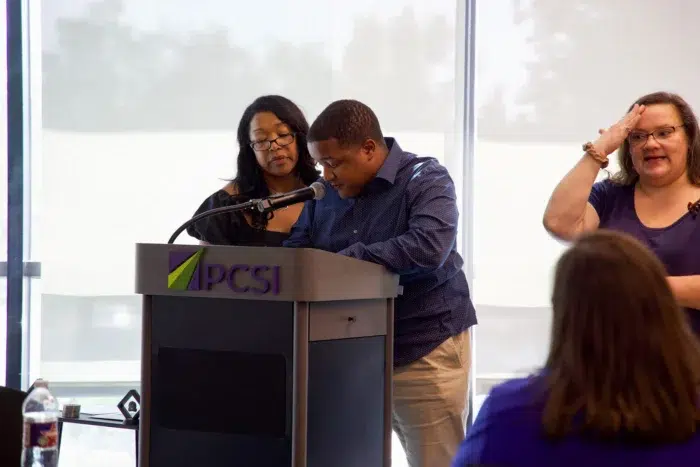 Special Olympics speaker presenting at PCSI branded podium with mother and ASL translator at his side.